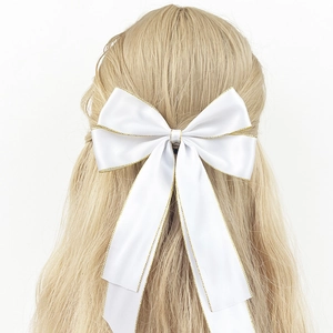 Close-up of white silk bow hair clip with gold glitter trim worn on model's hair
