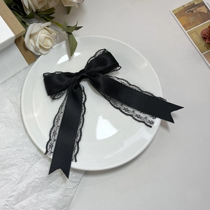 Detailed view of a black satin hair bow with delicate lace trim on a vintage background