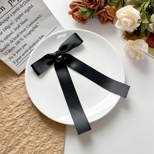 Pince à cheveux nœud en satin noir avec rubans longs sur une assiette décorative