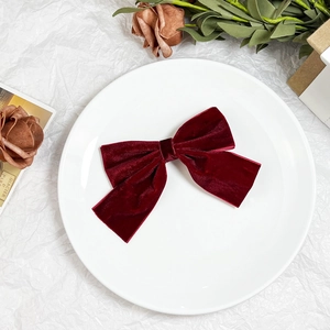 Detailed view of a vintage burgundy velvet bow hair clip on a white decorative plate