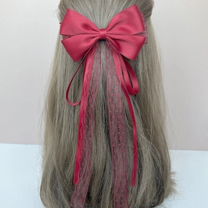 Detail of red satin bow hair clip with lace ribbons on a long flowing streamer
