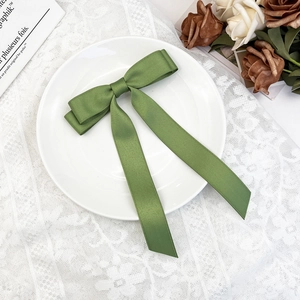 Detail of elegant dark green satin bow hair clip with long ribbons on white plate