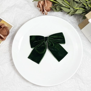 Detailed close-up of dark green velvet bow hair clip with vintage texture on a ceramic plate