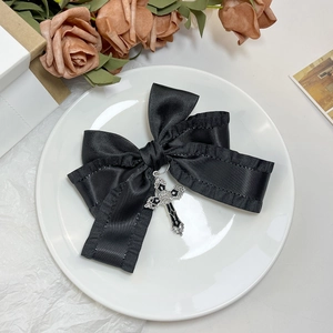 Détail de la pince à cheveux nœud en satin noir avec un pendentif croix gothique argenté