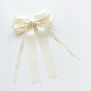 Detailed view of layered cream satin bow hair clip with elegant long ribbons and silky texture