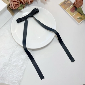Detail of elegant black satin ribbon bow hair clip on a white ceramic plate with dried flowers