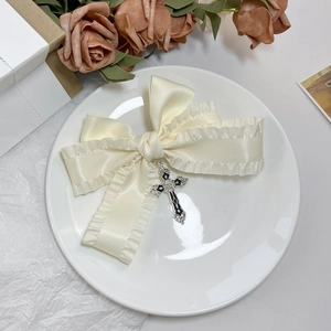 Détail d'un nœud papillon en satin crème avec pendentif croix noire sur assiette décorative