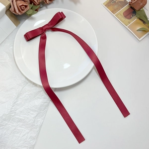 Close-up of wine red silk satin bow hair clip with long ribbons on elegant decor