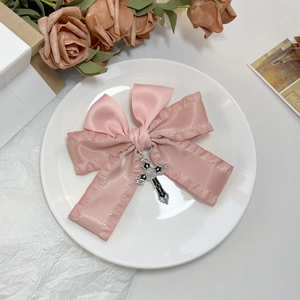 Détail d'un nœud en satin rose avec pendentif croix gothique sur une assiette décorative