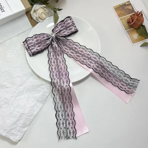 Detail of pink satin bow hair clip with black lace overlay and heart-shaped gemstone