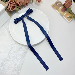 Close-up of a navy blue ribbon bow hair clip with long streamers on a white ceramic plate