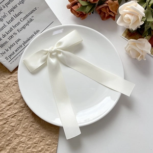 Détail d'une barrette à nœud en satin crème avec rubans sur une assiette en céramique