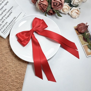 Close-up of elegant red satin bow hair clip with long ribbons on a white porcelain plate