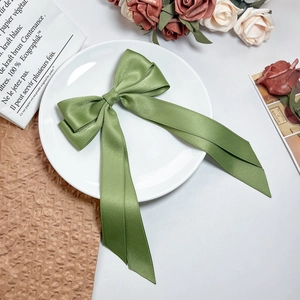 Detailed view of an olive green satin ribbon hair bow on a white vintage ceramic plate