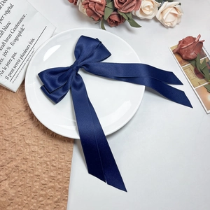 Macro detail of a navy blue satin bow hair clip with long ribbons on a white ceramic plate