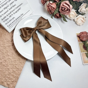 Detail of coffee brown satin bow hair clip with elegant ribbons on white ceramic plate