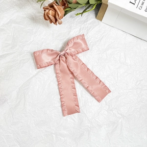 Detail of light pink satin bow hair clip with ruffled edges on aesthetic white background
