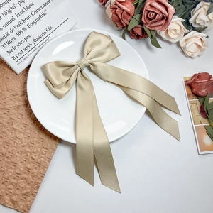 Detail view of champagne gold satin bow hair clip with ribbons on white ceramic plate