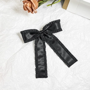 Detail of black satin bow hair clip with ruffled edges and elegant long ribbons
