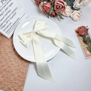 Close-up of elegant cream satin bow hair clip with long ribbons on a decorative plate