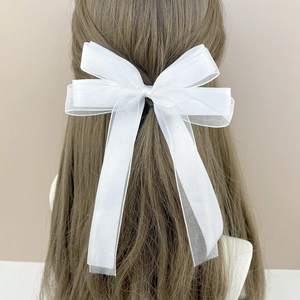 Elegant white mesh bow hair clip with long flowing ribbons on a brunette model
