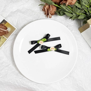 Detailed view of two black ribbon bow hair clips with cream roses and green leaves on a tray