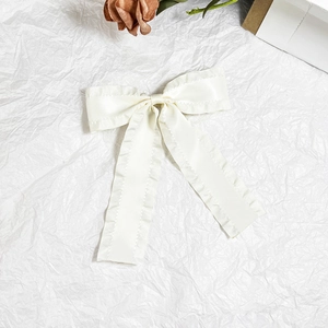 Detail of a creamy white satin bow hair clip with ruffled edges and elegant long ribbons