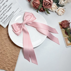 Elegant pink satin bow hair clip with long ribbons on a decorative white display plate