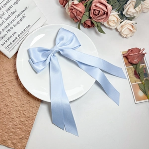 Detail view of a light blue satin bow hair clip with elegant long ribbons on a white plate