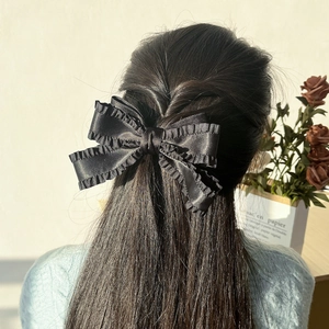 Détail d'une grande pince à cheveux en satin noir à volants pour demi-queue de cheval