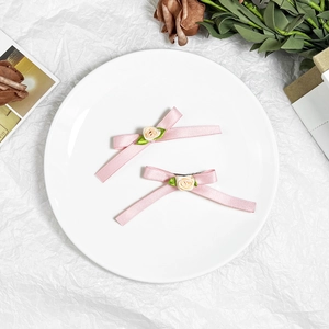 Pink ribbon bow hair clips with rose and green leaves on white ceramic plate