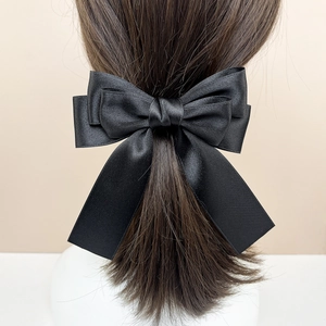 Detail of multi-layered black satin bow hair clip with long ribbons on a model back