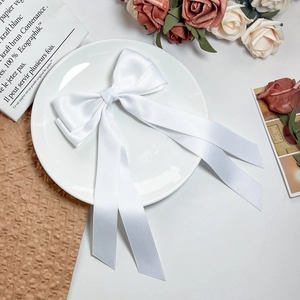 Elegant white satin bow hair clip with long ribbons on a vintage decorative tray