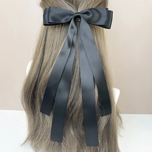Elegant black satin bow hair clip with long ribbons for women, shown on hair