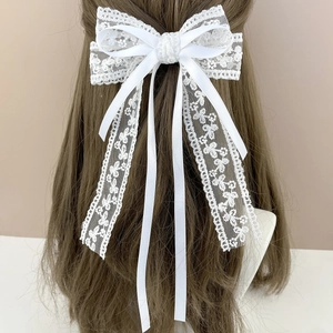 Elegant white lace bow hair clip with long ribbons worn by a model in a soft setting