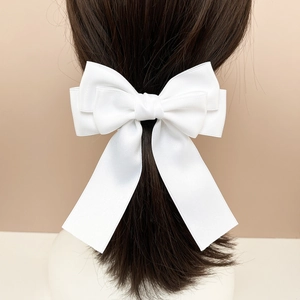 Macro detail of multilayer white satin bow hair clip with long ribbons on dark hair