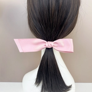 Detailansicht einer rosa Satin-Schleife-Haarspange in einem schwarzen Pferdeschwanz