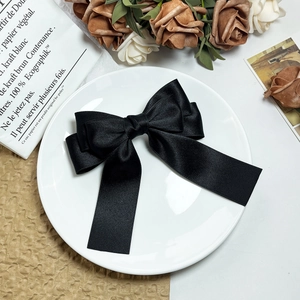 Detail of multi-layered black grosgrain ribbon bow hair clip on a minimalist white plate