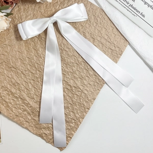 Detail of elegant white satin ribbon hair clip with long streamers on dark paper background