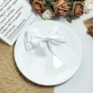 Elegant white layered satin bow hair clip placed on a decorative ceramic plate