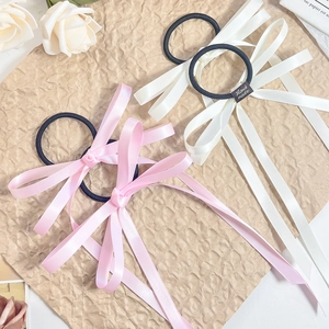 Close-up of pink and cream satin bow hair ties with long ribbons on textured paper