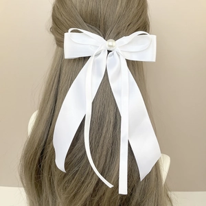 Détail d'une pince à cheveux en satin blanc avec perle et longs rubans fluides