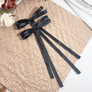 Detail of elegant black satin bow hair clip with long ribbons on vintage paper background