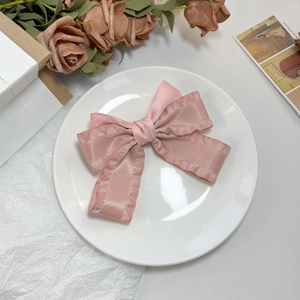 Détail d'une pince à cheveux à nœud en satin rose avec ruban plissé sur une assiette blanche