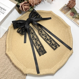 Elegant black lace and satin bow hair clip with long ribbons on a vintage tray