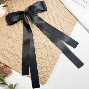 Detail of a large black satin bow hair clip with long ribbons on vintage paper