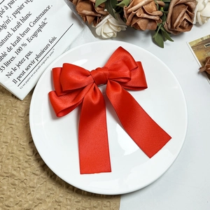 Close-up of red multilayer satin bow hair clip with ribbons on elegant background