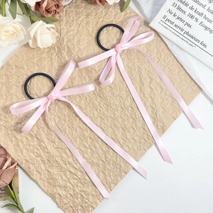 Pink ribbon bow hair ties with long streamers on textured paper with white roses