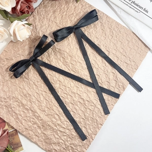 Macro detail of two black satin ribbon bow hair clips on aesthetic vintage paper