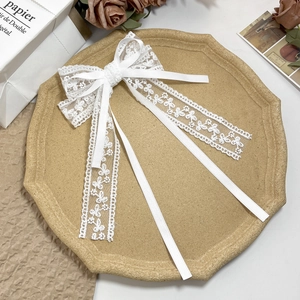 Detail of elegant white lace bow hair clip with long ribbons and floral embroidery
